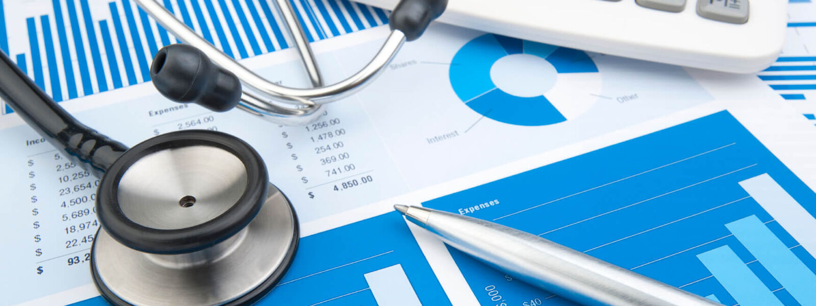 Close-up photo of a stethoscope calculator and pen on a piece of paper with graphs printed on it