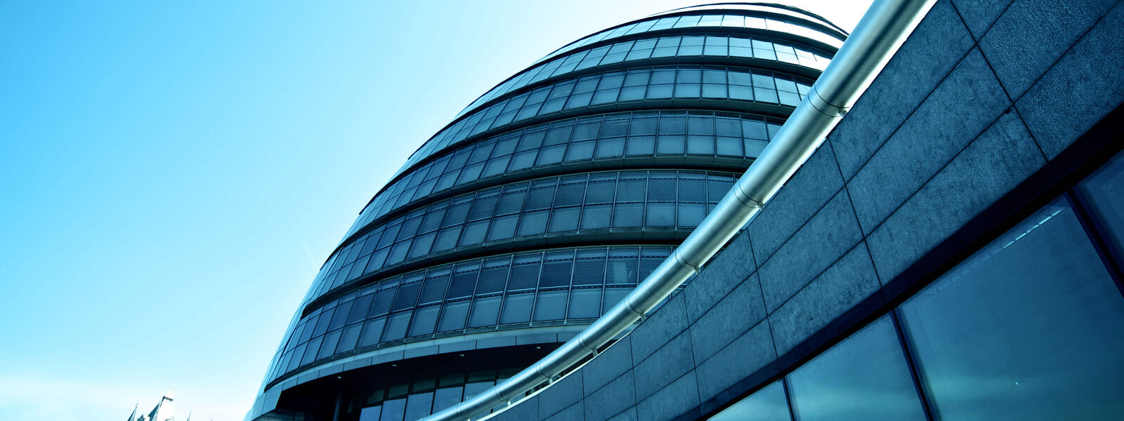 A photo taken at street-level of a dark grey building with floor-to-ceiling windows, clear blue sky