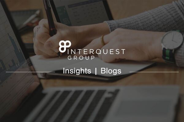 A insights banner image for a blog with the InterQuest Group logo on a image of a person writing notes from two screens