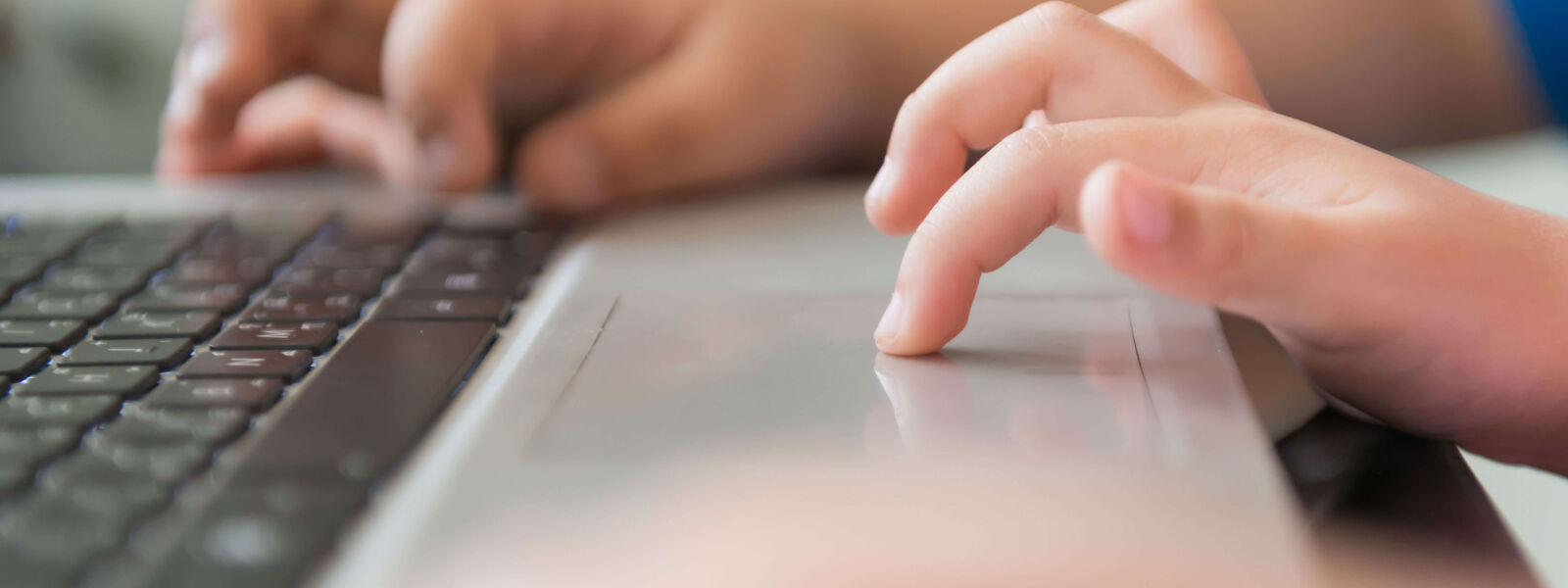 A pair of small hands using a laptop, one finger on the trackpad