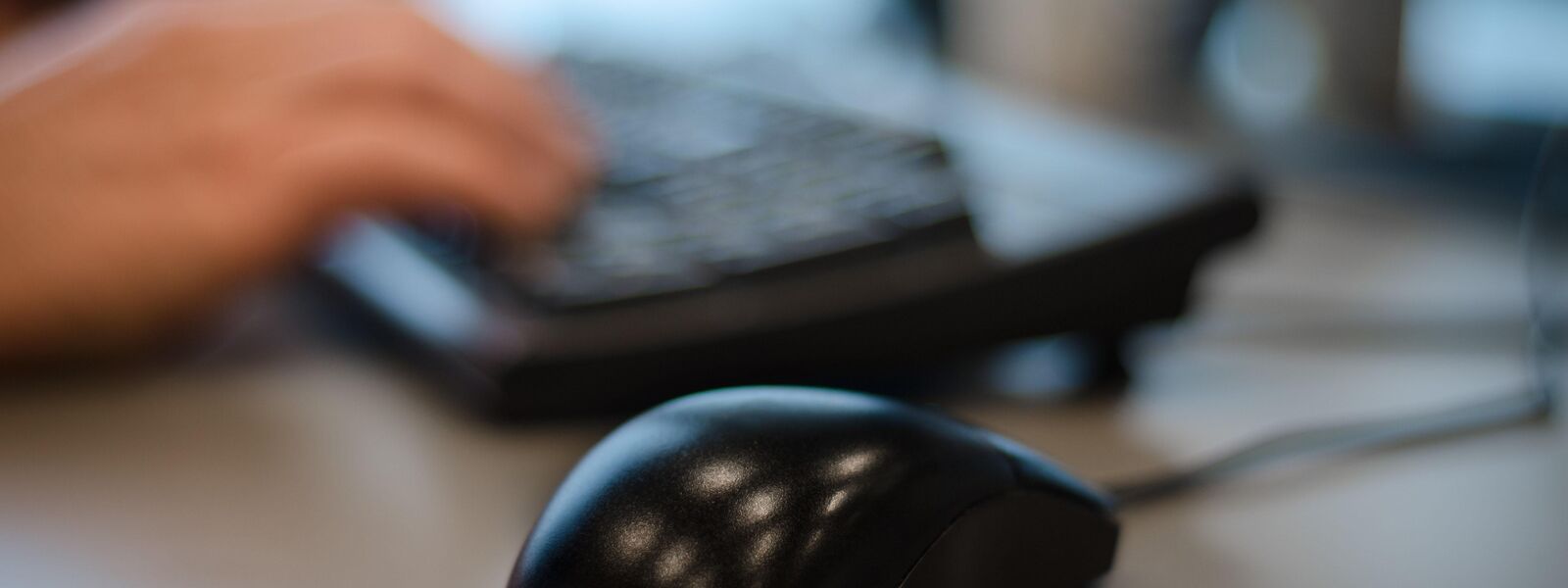 Close-up of a computer mouse with a person using a keyboard blurred in the background
