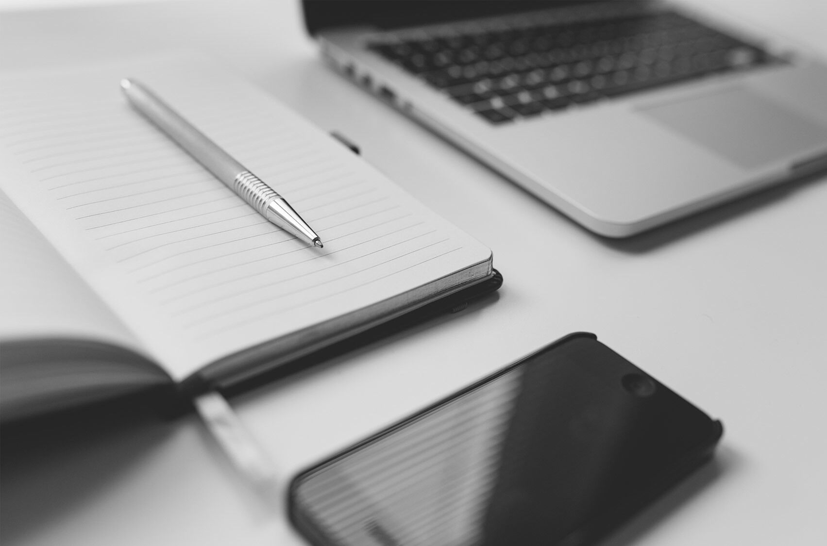 A phone, notepad and laptop on a white table