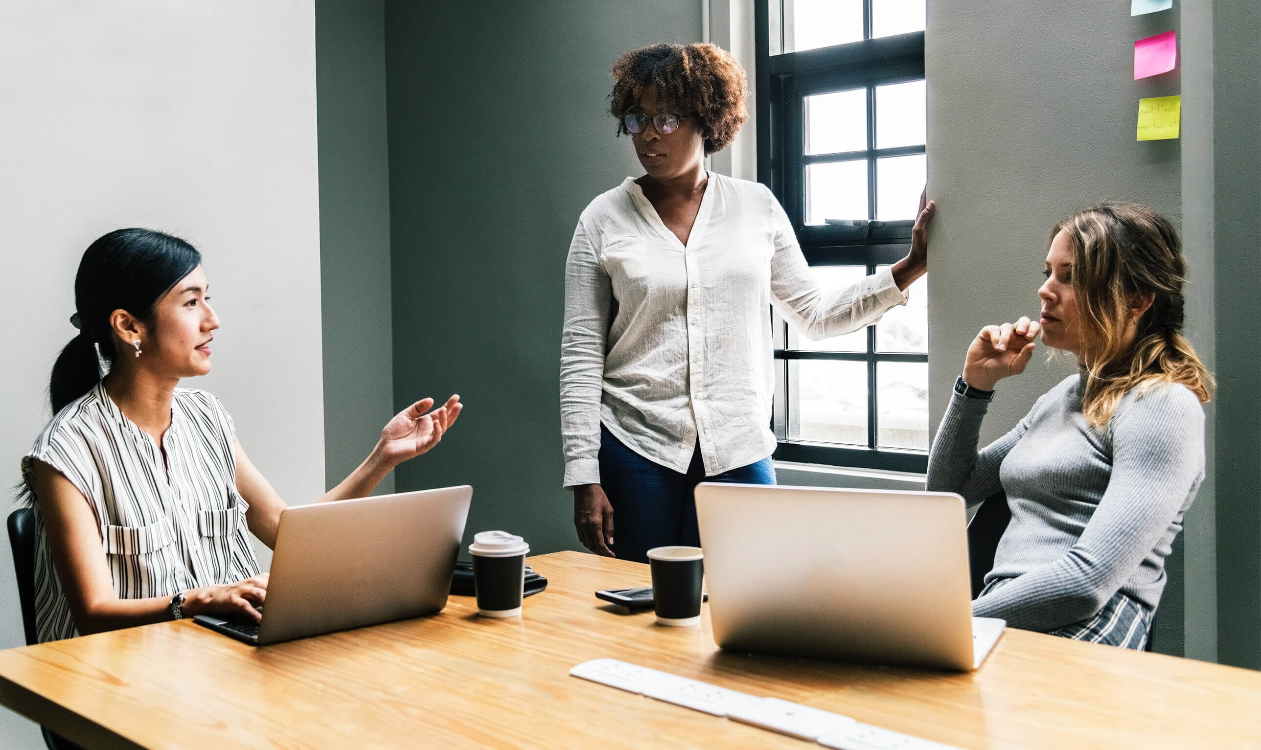 Three people in a discussion around a table with post-it notes on the wall