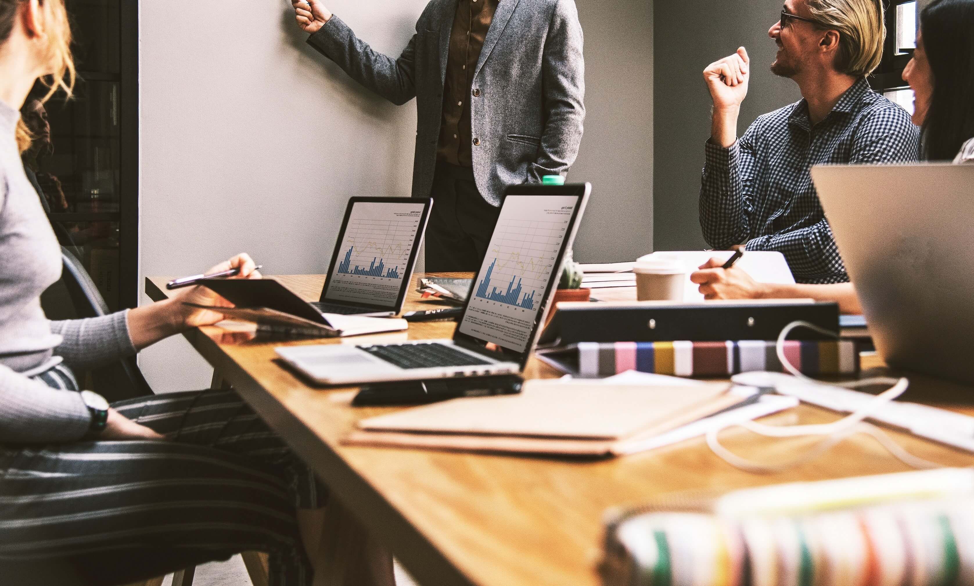 Cropped photo of people in a business meeting, laptops, charging cables and paper folders on the table