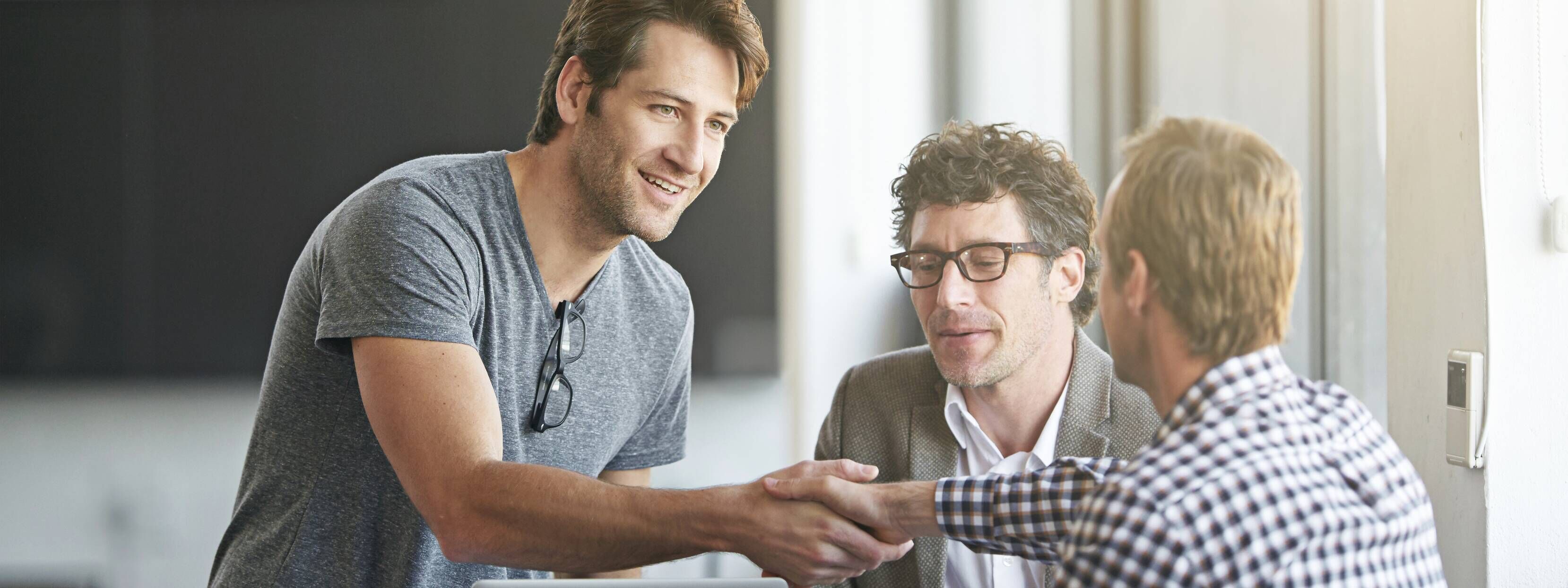 Three people having a meeting two are greeting by shaking hands