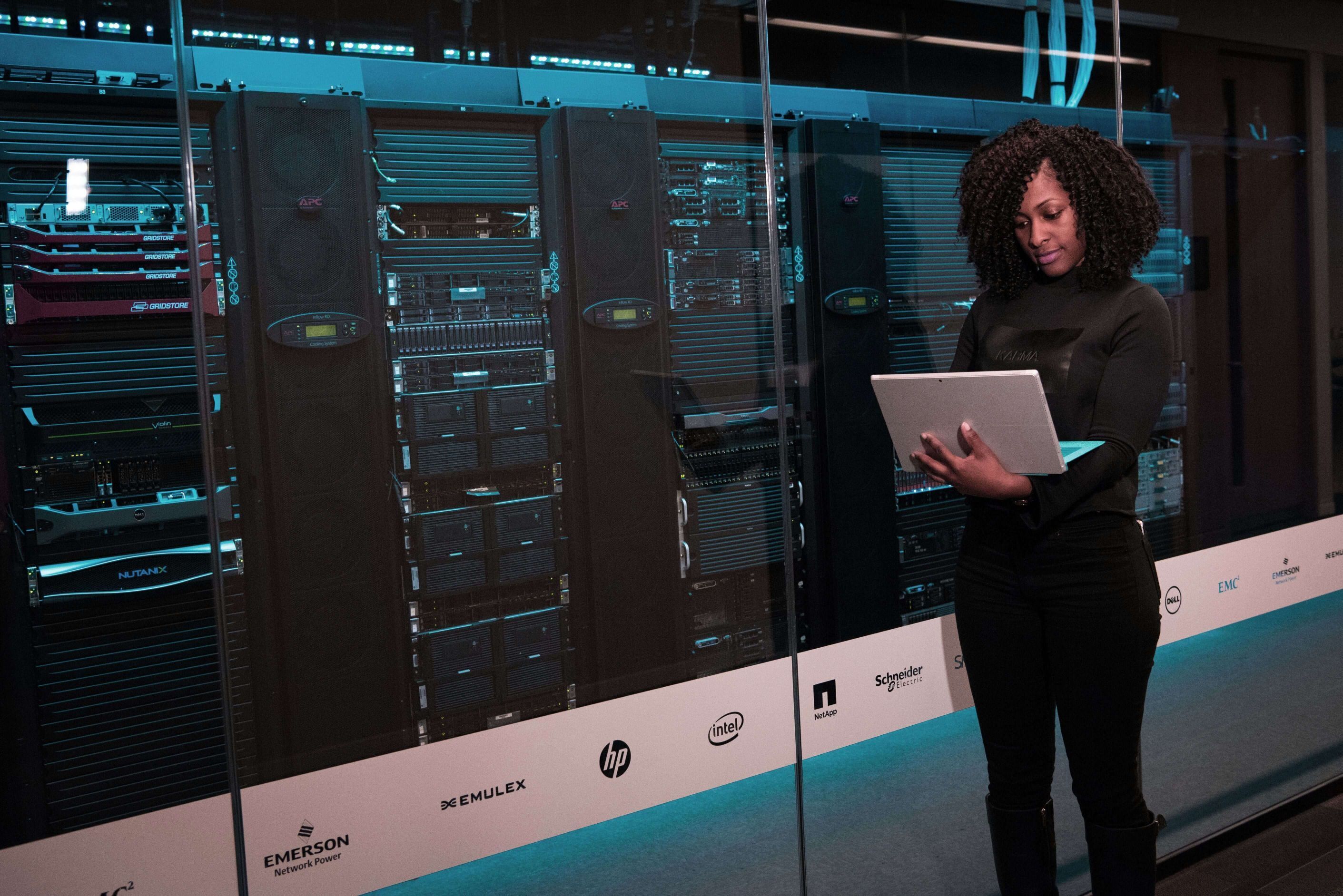 A stock photo of a person using a laptop while standing in a data center