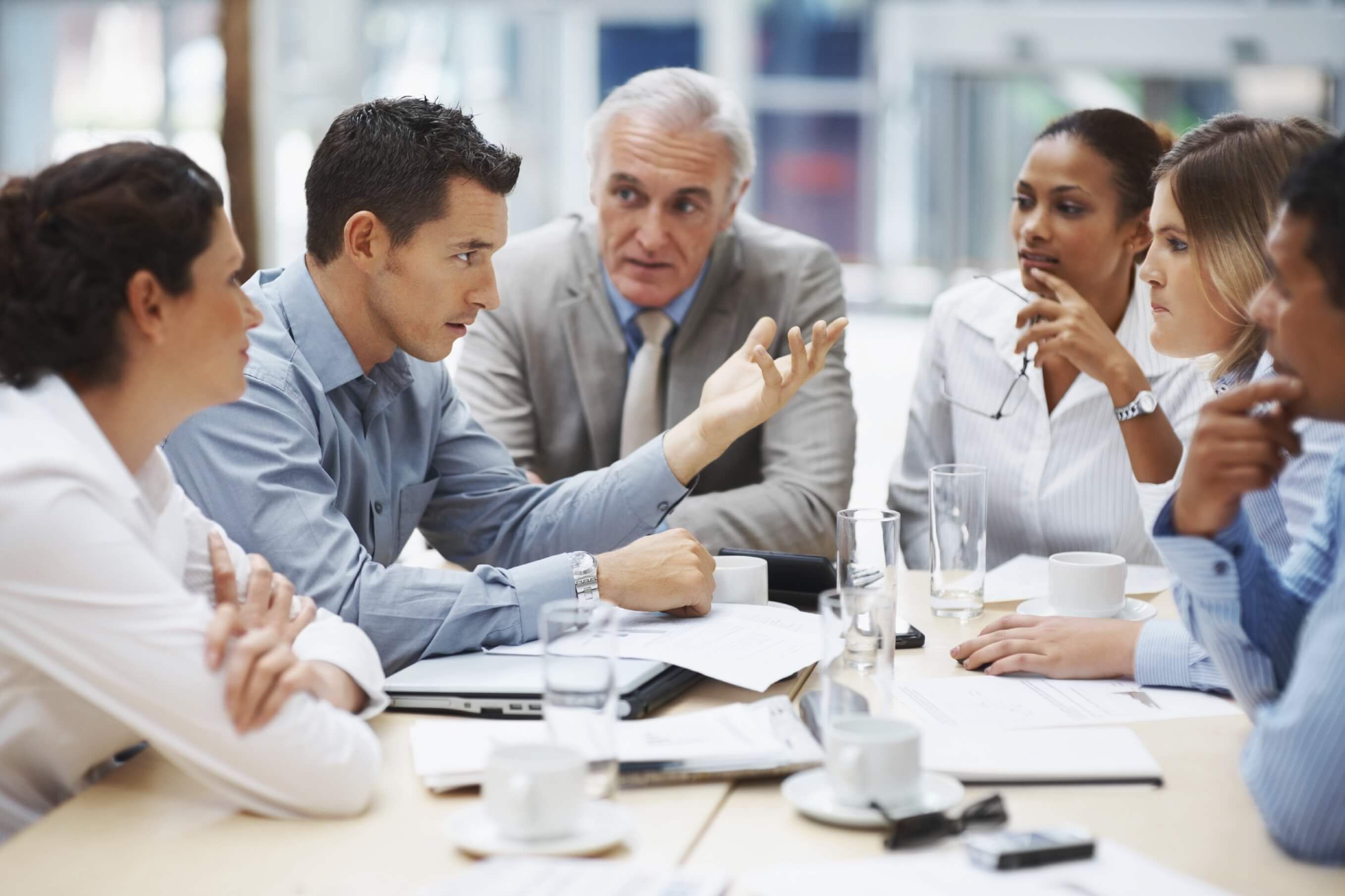 A stock photo of six people huddled around a table in a discussion