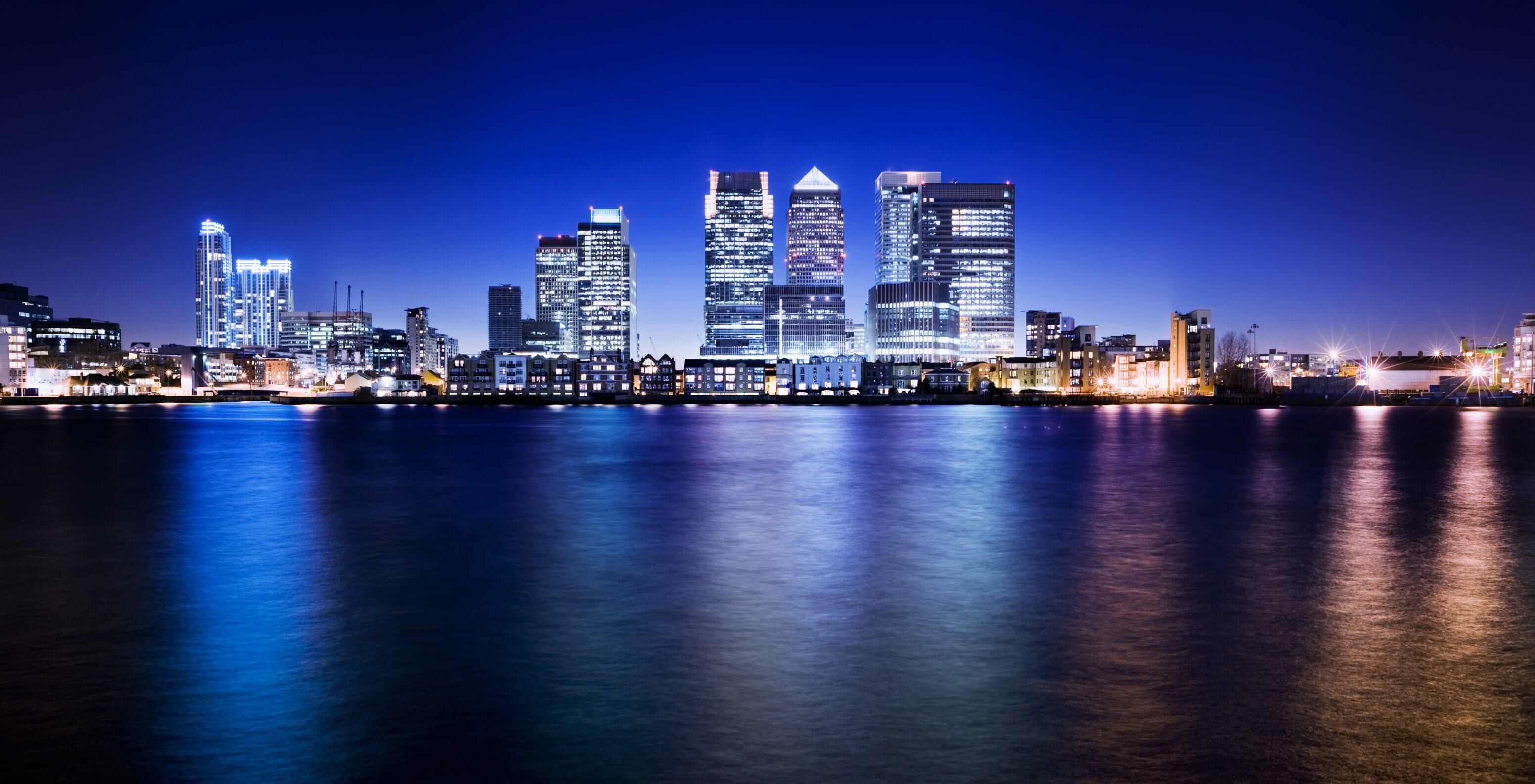 A city landscape photo at night with glow reflected in water