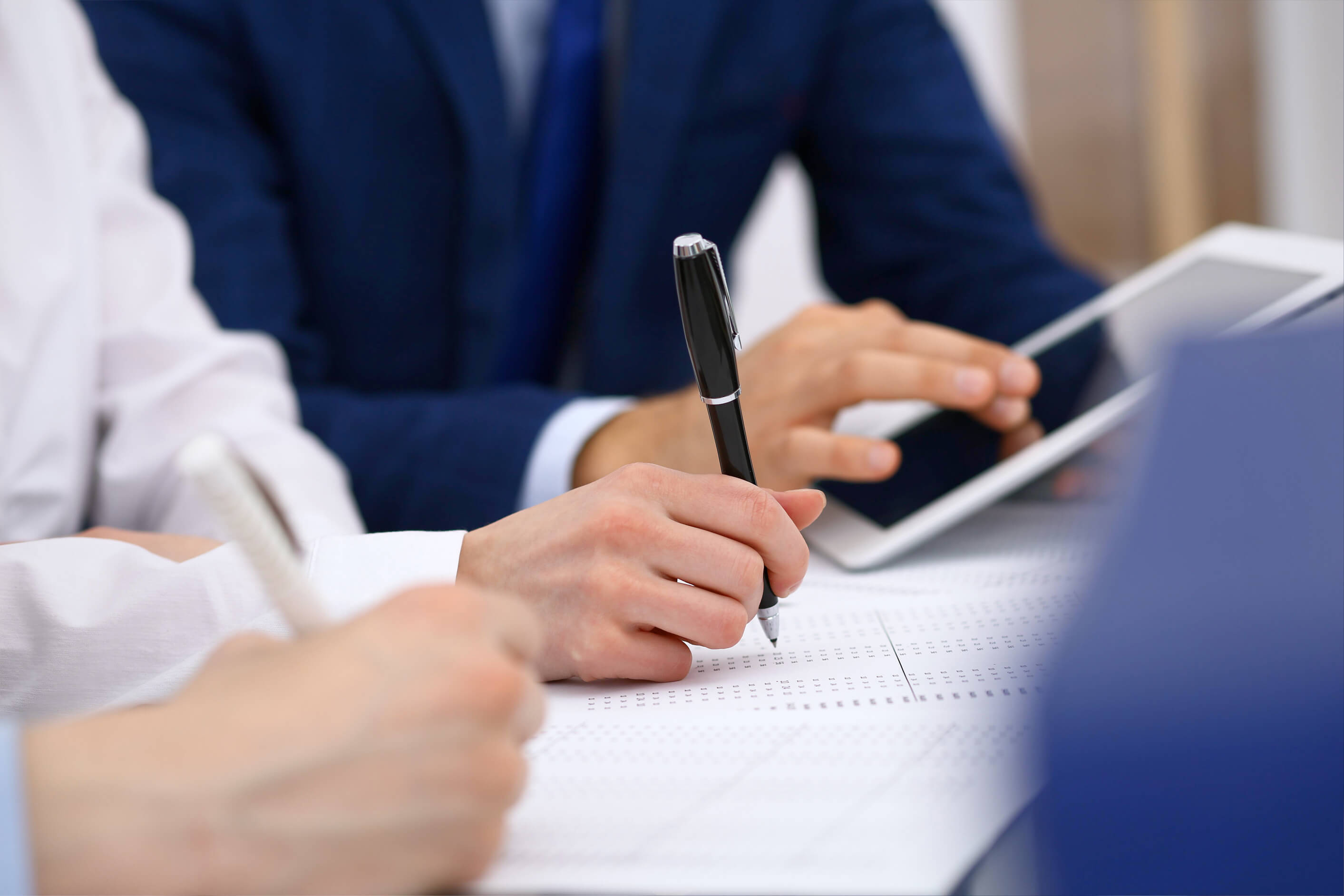 Three people in business attire sat at a desk sharing information on paper and a tablet