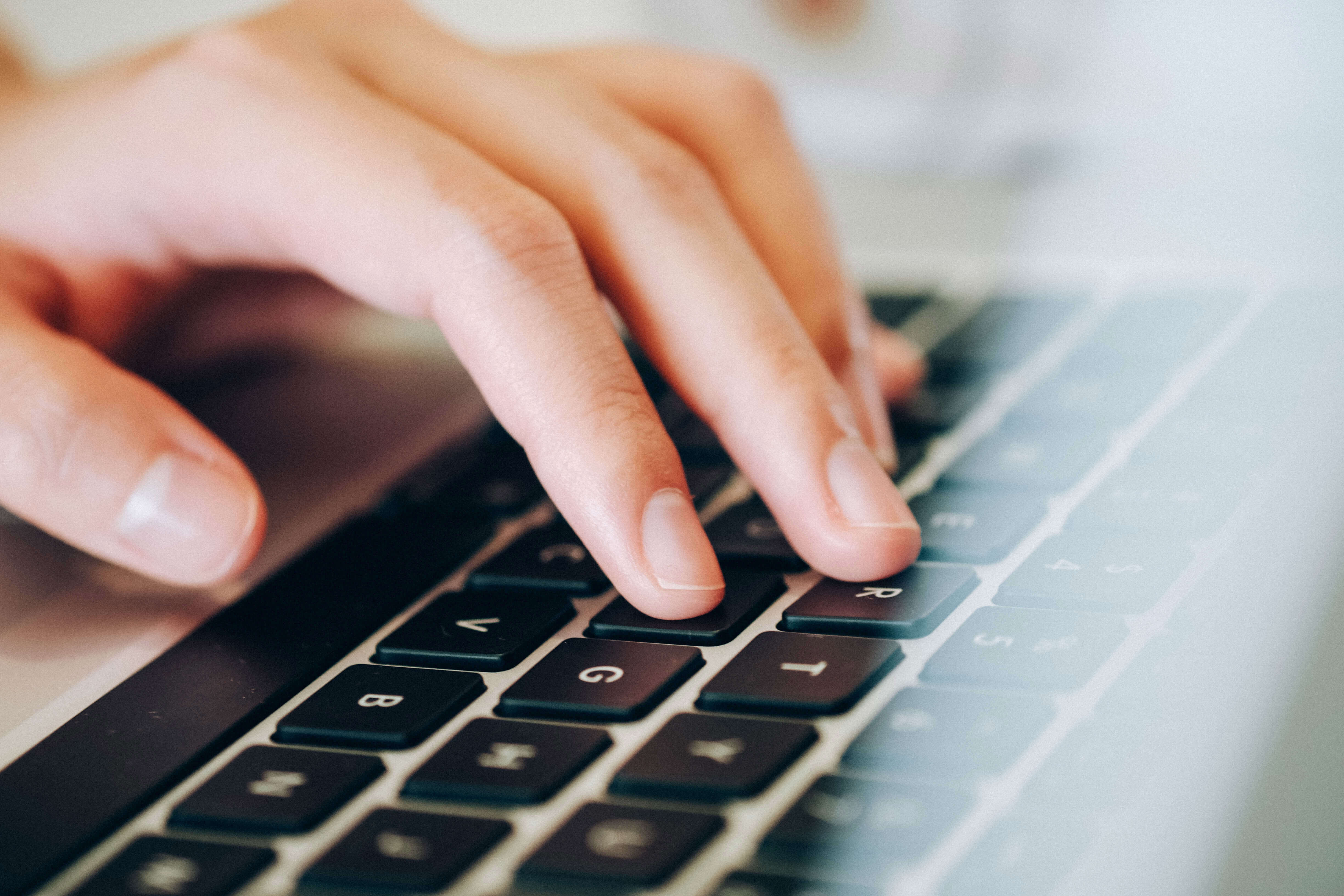 A close-up of a hand typing on a laptop keyboard