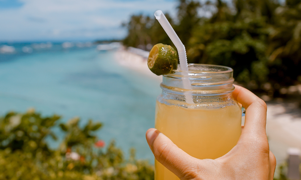 A hand holding a tropical drink on a beach in the sun