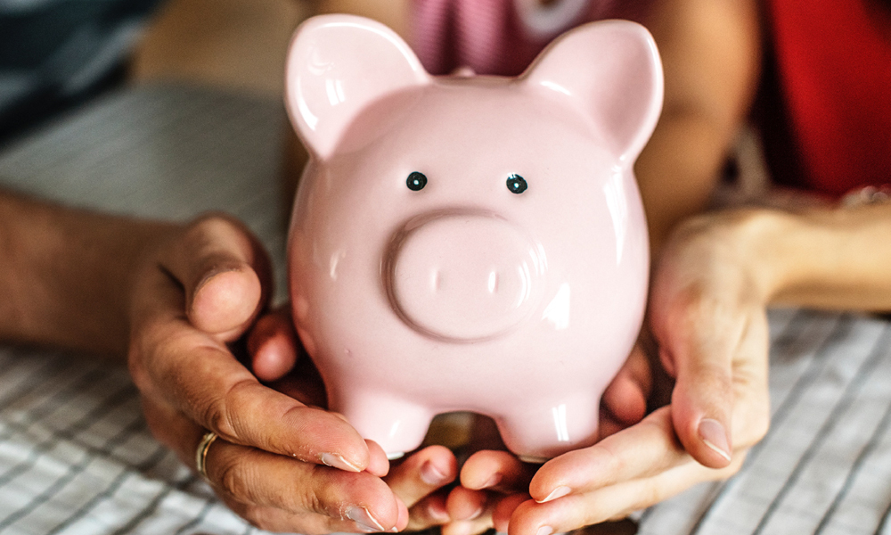 Pairs of hands holding a 'piggy bank' resting on a table