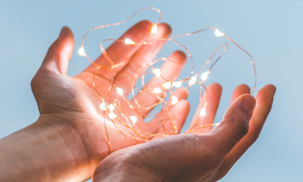 Photo of a pair of hands loosely holding fairy-lights blue background