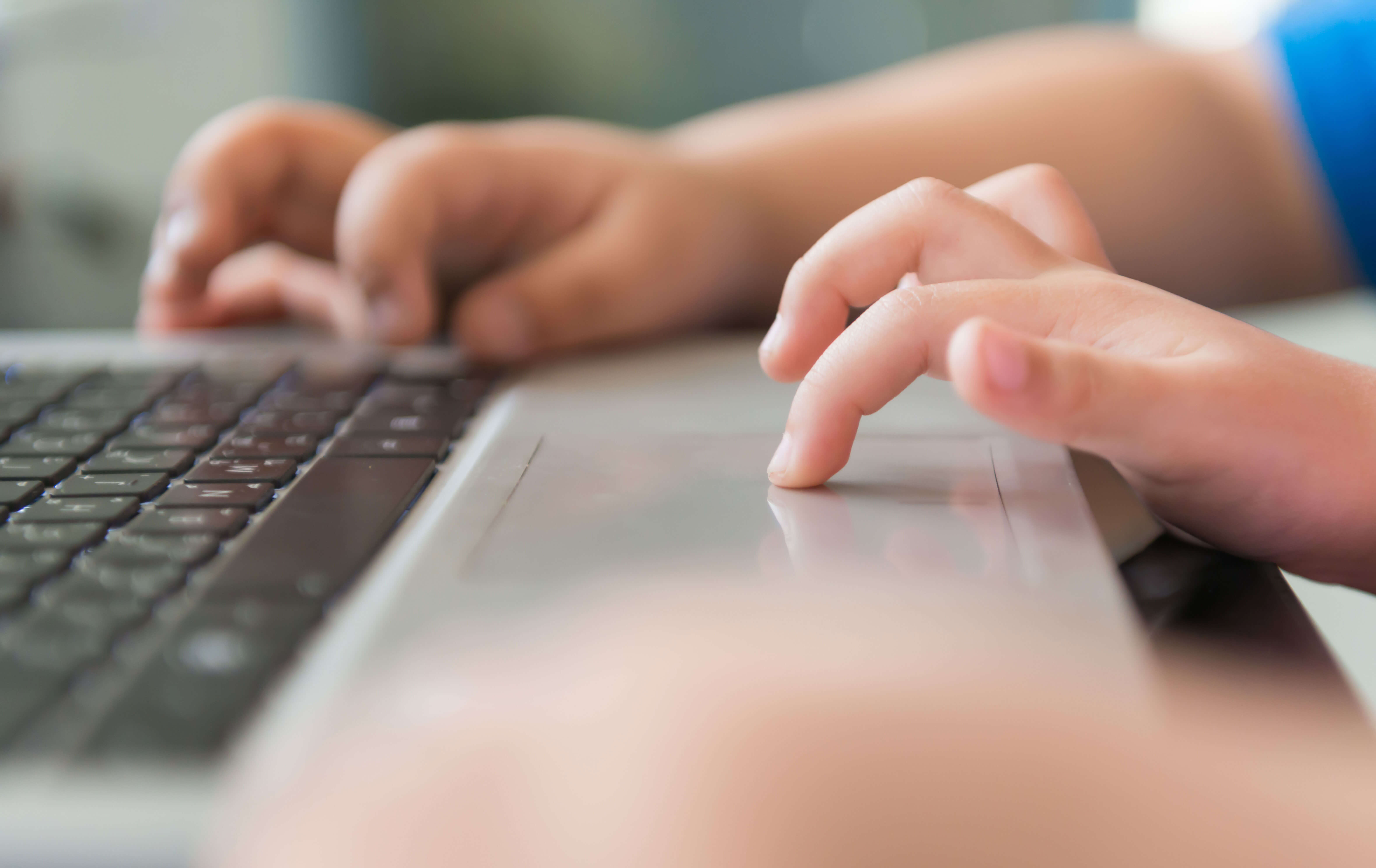 A pair of small hands using a laptop, one finger on the trackpad